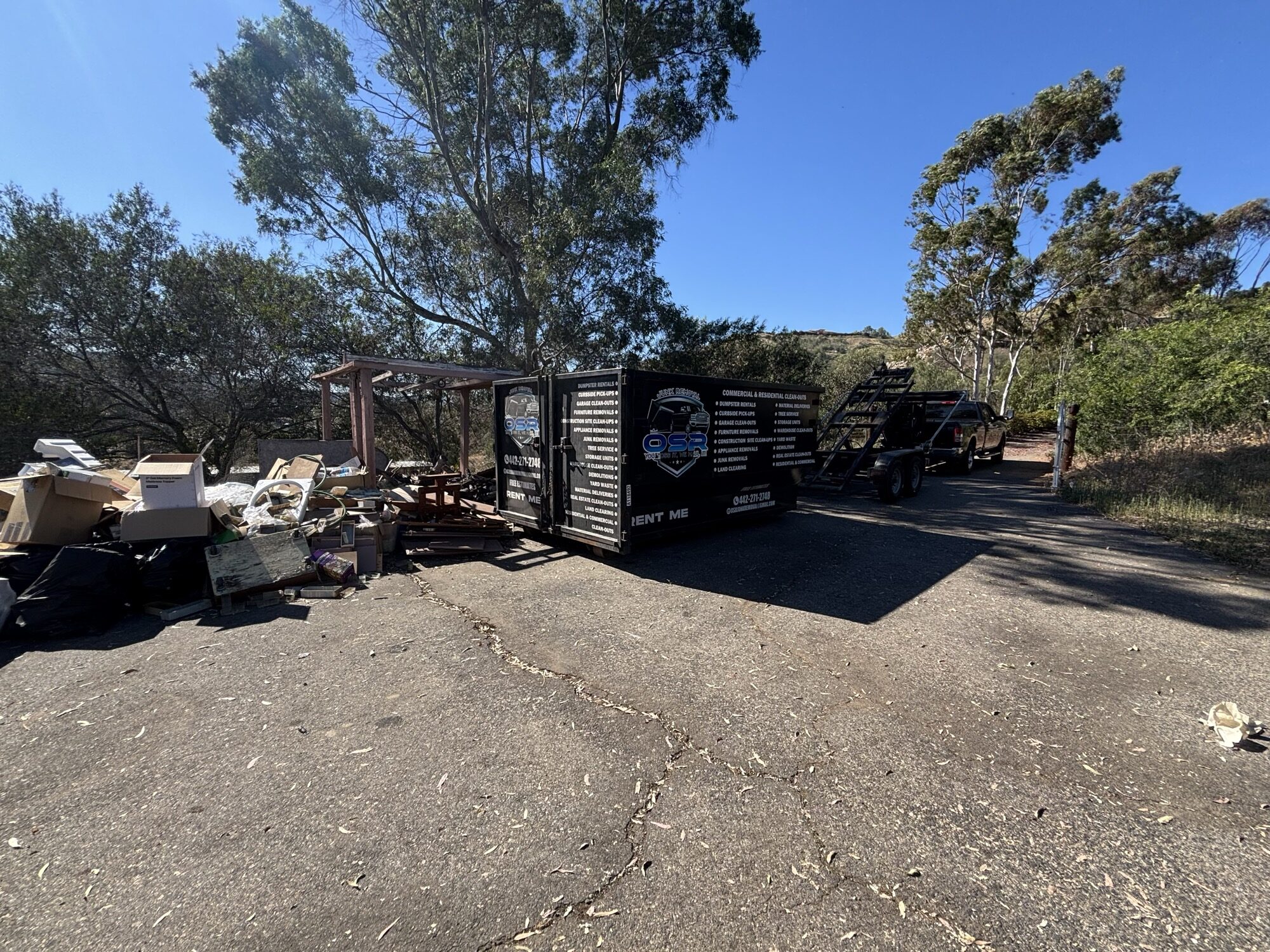 Black roll-off dumpster loaded with tree branches and brush at a Fallbrook property clearing job
