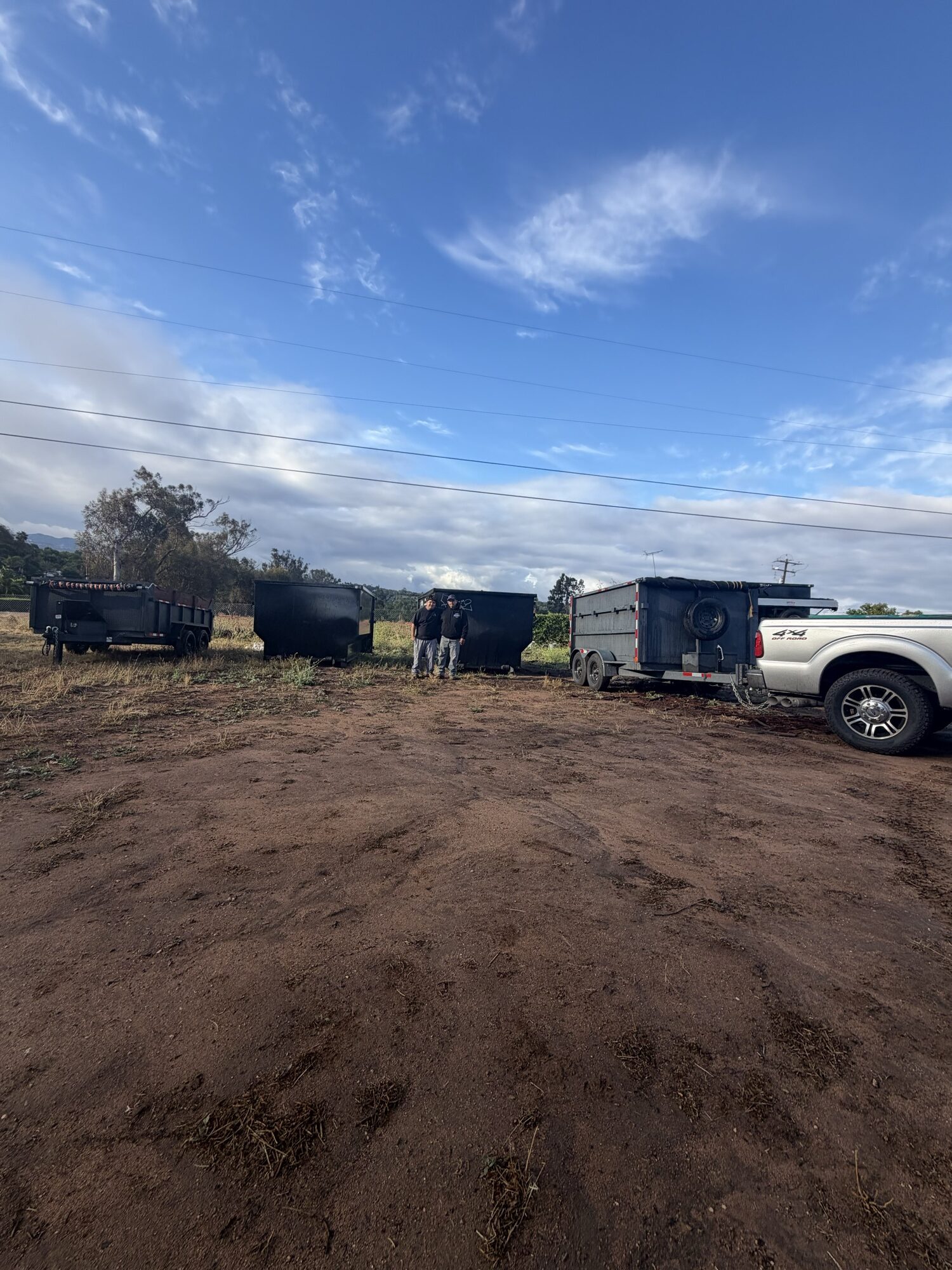 Oscar and Oscar Sr., the family owners of OSR, standing between their dumpsters and hauling truck on a cleared job site in Fallbrook, CA — serving Fallbrook, San Diego County